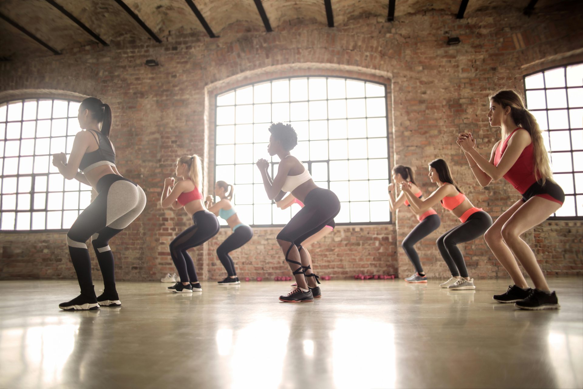 Mujeres participando en una clase de fitness grupal realizando sentadillas en un estudio de estilo industrial.