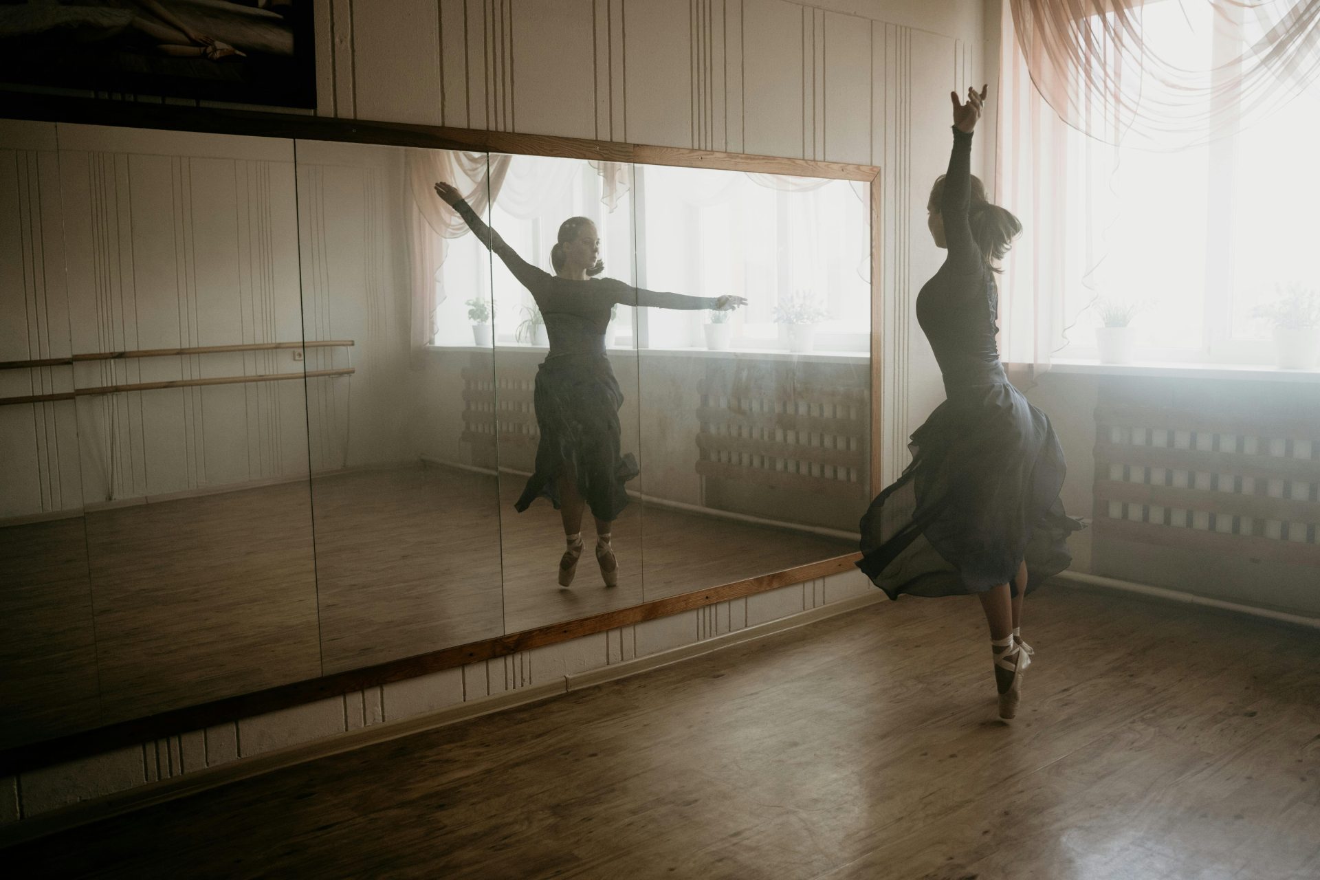 Una elegante bailarina danza de puntillas en un estudio iluminado por el sol, capturando el movimiento y el reflejo.
